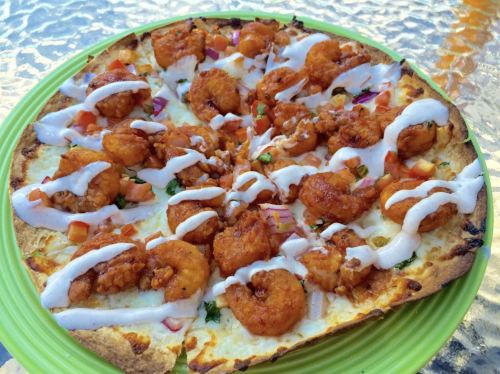 A pizza topped with shrimp, diced tomatoes, onions, and drizzled with white sauce on a green plate.