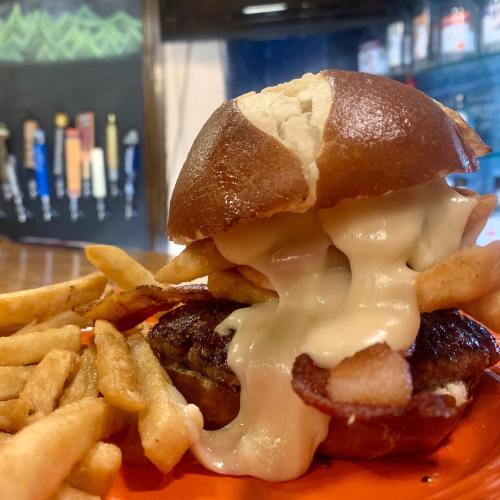 A close-up of a pretzel bun burger with melted cheese and fries on an orange plate.
