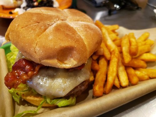 A juicy burger with melted cheese, bacon, and lettuce, served with a side of crispy fries on a paper tray.