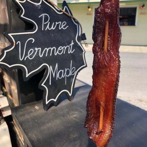 A piece of maple candy on a stick next to a sign that reads "Pure Vermont Maple."