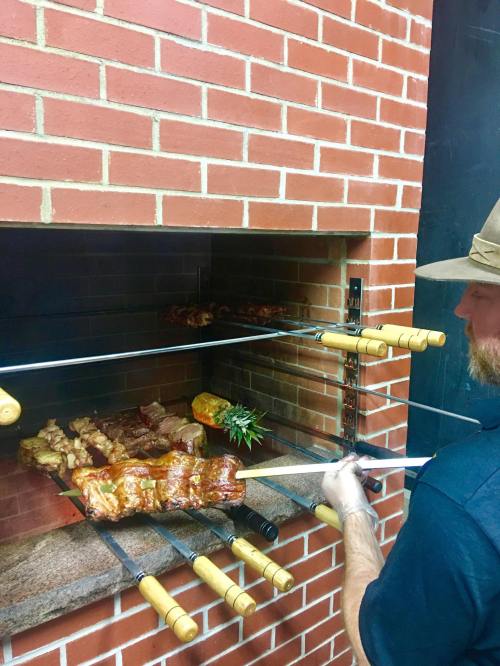 A person grilling skewers of meat over an open flame in a brick barbecue setup.