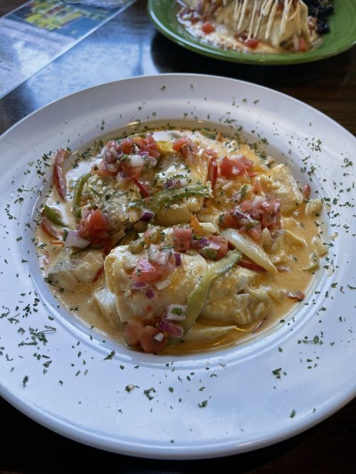 A plate of creamy pasta topped with diced tomatoes, green peppers, and herbs.