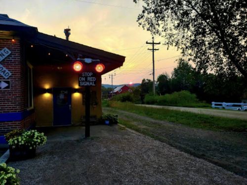 A quaint building with a stop signal, surrounded by greenery and a sunset sky in the background.