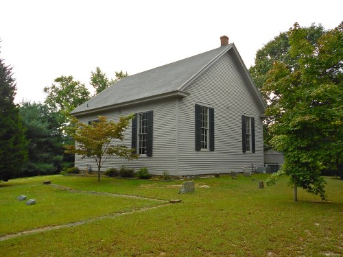 A gray house with black shutters, surrounded by green grass and trees, set in a peaceful outdoor environment.