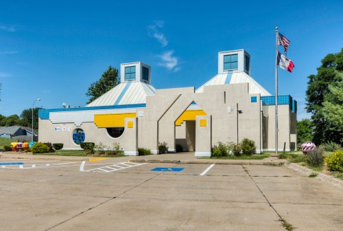 A modern building with a unique design, featuring blue and yellow accents, surrounded by a parking lot and trees.