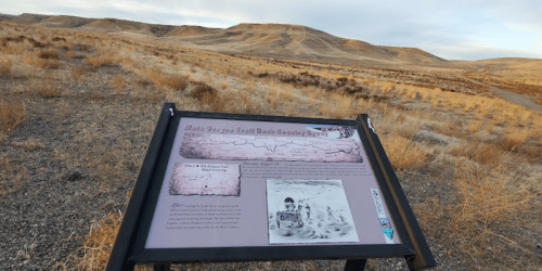 A historical sign about the Oregon Trail, set against a backdrop of rolling hills and sparse vegetation.