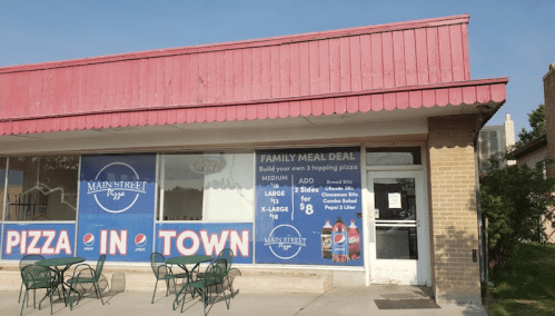 Exterior of a pizza shop with a pink awning, featuring a sign for a family meal deal and outdoor seating.
