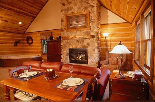 Cozy log cabin interior with a stone fireplace, dining table, and a relaxing hot tub in the background. Warm lighting.