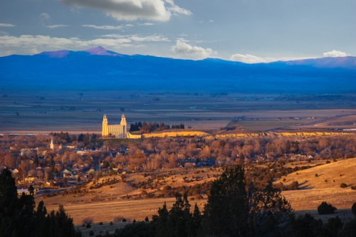 A scenic view of a valley with mountains in the background and a historic building in the foreground, bathed in golden light.
