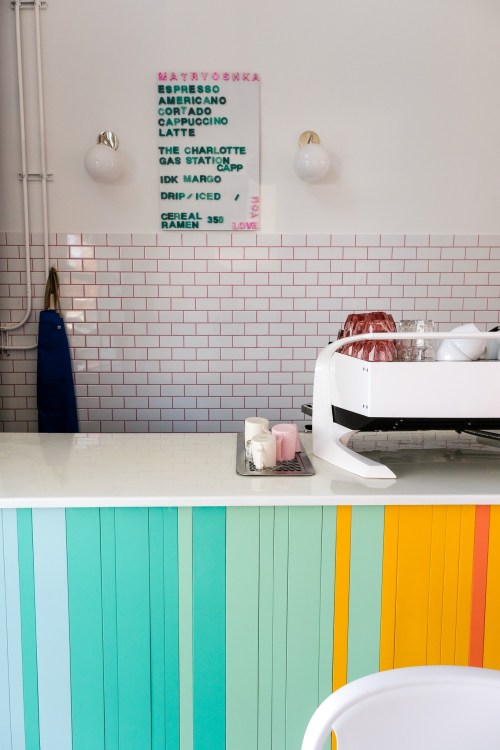 A colorful café counter with a menu board and coffee equipment, featuring pastel-colored vertical panels.