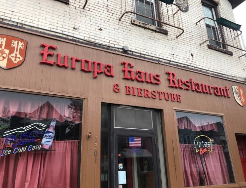 Sign for Europa Haus Restaurant & Bierstube, featuring red lettering on a brown facade with beer advertisements.