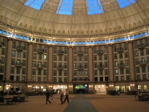 Interior view of a grand atrium with a high dome, featuring multiple floors of balconies and soft lighting.