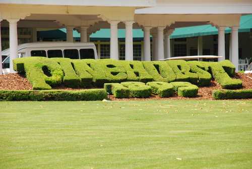 Topiary letters spelling "Pinehurst" in green bushes, set on a manicured lawn with a building in the background.