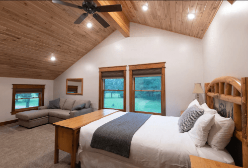 Cozy bedroom with wooden accents, a large bed, a sofa, and windows overlooking a green landscape.