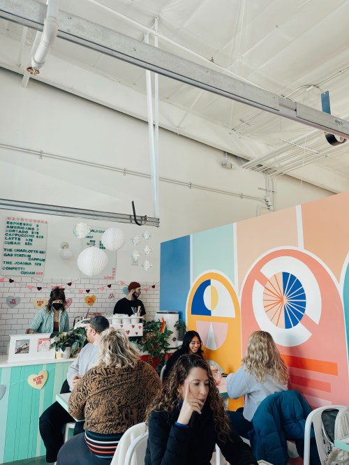 A vibrant café interior with colorful walls, patrons enjoying their time, and staff serving at the counter.