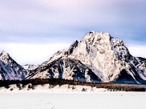 Snow-covered mountains rise majestically against a cloudy sky, reflecting serene winter beauty.