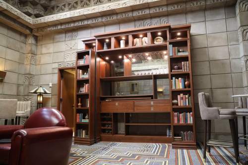 A wooden bookshelf with books and decorative items, set in a stylish room with patterned flooring and modern furniture.