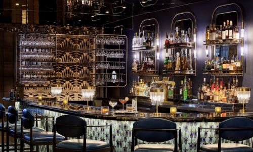 A stylish bar with a sleek design, featuring shelves of liquor, elegant glassware, and ambient lighting.