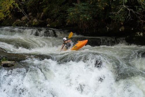 A kayaker navigates through turbulent whitewater rapids, surrounded by lush greenery.