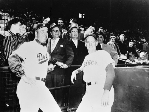 Two baseball players in uniforms pose in front of a crowd, smiling, with fans and spectators in the background.