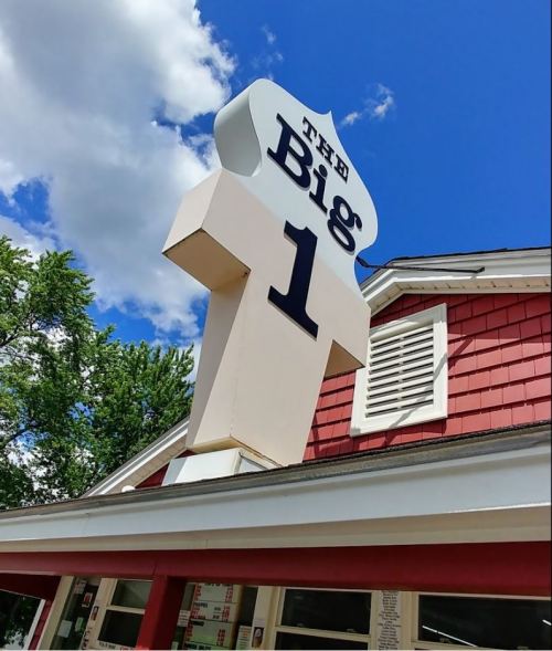 Sign for "The Big 1" restaurant against a blue sky with clouds, atop a red and white building.