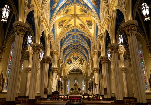 Interior of a grand church featuring ornate blue and gold ceilings, tall columns, and stained glass windows.