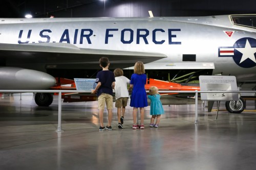 Four children stand in front of a U.S. Air Force aircraft, admiring it in a museum setting.