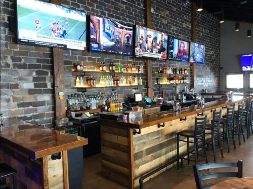 A rustic bar with multiple TVs showing sports, shelves of liquor, and wooden seating in a cozy atmosphere.