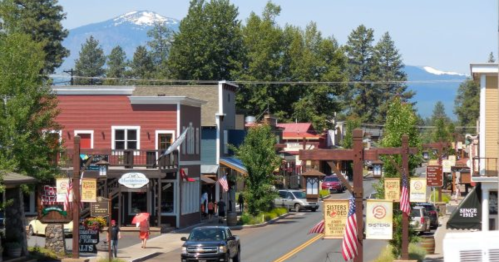 A charming small town street lined with shops, trees, and mountains in the background on a sunny day.