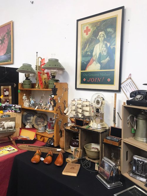 A display of various antiques and collectibles, including ships, figurines, and a vintage poster on the wall.