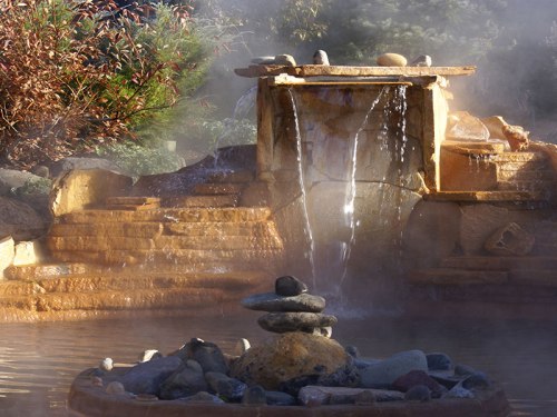A serene stone fountain with cascading water, surrounded by mist and smooth pebbles, set in a tranquil garden.