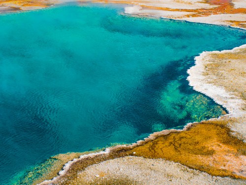 Vibrant turquoise hot spring surrounded by mineral-rich, colorful terrain in a natural landscape.