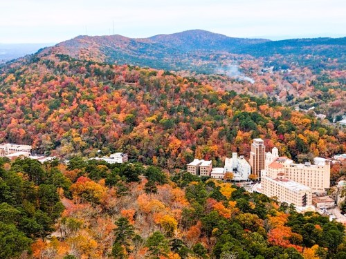 Aerial view of a colorful autumn landscape with hills, trees, and a small town nestled at the base.