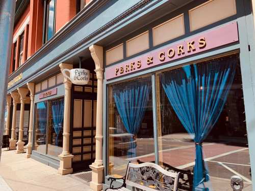 Exterior of a café named "Perks & Corks," featuring large windows with blue curtains and a decorative façade.