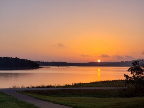A serene sunrise over a calm lake, with soft orange and pink hues reflecting on the water's surface.