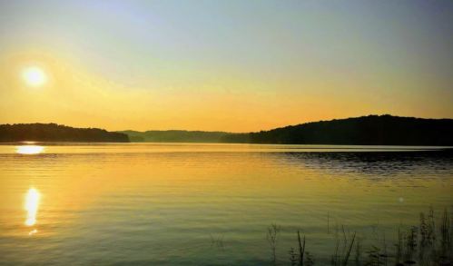 A serene lake at sunset, reflecting golden hues with distant hills and a clear sky.