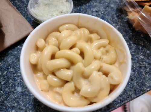 A cup of creamy macaroni and cheese with spiral pasta, served on a blue countertop.