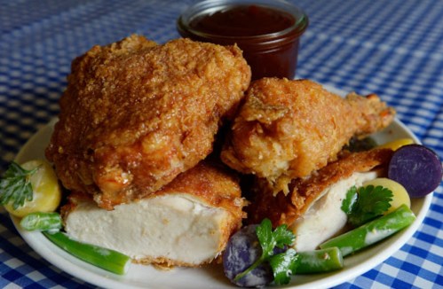 A plate of crispy fried chicken pieces with a side of colorful vegetables and a small jar of barbecue sauce.