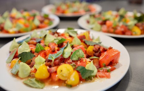 Colorful salad with tomatoes, bacon, and green herbs, served on white plates.