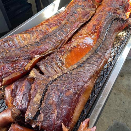 Smoked meat on a grill, showcasing a rich, dark crust and juicy texture, resting on a metal tray.