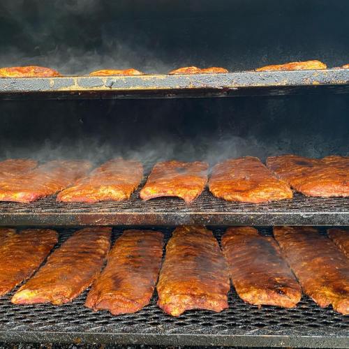 Smoky barbecue ribs cooking on racks inside a smoker, with steam rising and a rich, caramelized glaze.