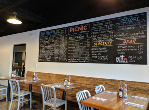 Chalkboard menu at a restaurant featuring beer, burgers, sides, desserts, and specials, with wooden tables and chairs.