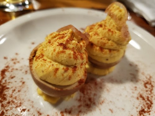 Two deviled eggs topped with paprika, served on a white plate with a sprinkle of seasoning.