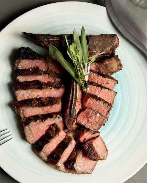 A beautifully plated steak, sliced and garnished with herbs, showcasing a perfect sear and juicy pink interior.