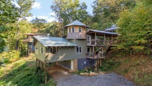 A unique multi-level house nestled in a wooded area, featuring a tower and a spacious deck.