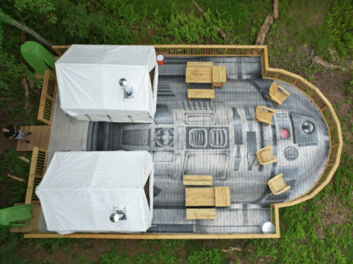 Aerial view of a unique outdoor space with two white tents and wooden tables, designed to resemble a spaceship interior.
