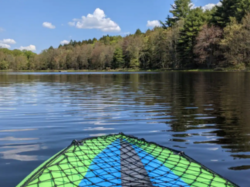 A vibrant kayak on calm water, surrounded by lush trees and a clear blue sky with fluffy clouds.