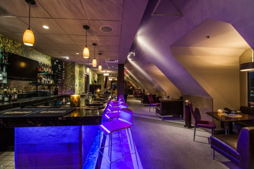 A stylish bar interior with modern seating, dim lighting, and a sleek counter, creating a cozy atmosphere.