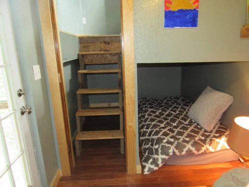 Cozy room with a small staircase leading to a bed, featuring wooden steps and a patterned blanket.