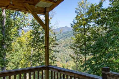 A scenic view from a wooden deck overlooking lush green mountains and trees under a clear blue sky.